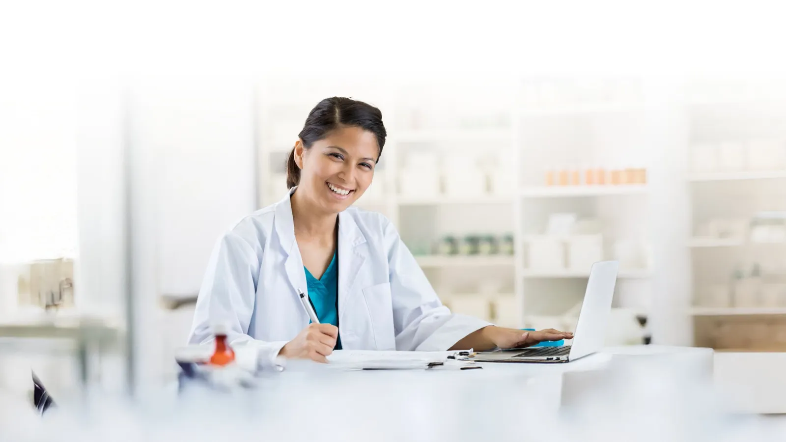A clinician smiling at her desk with a laptop