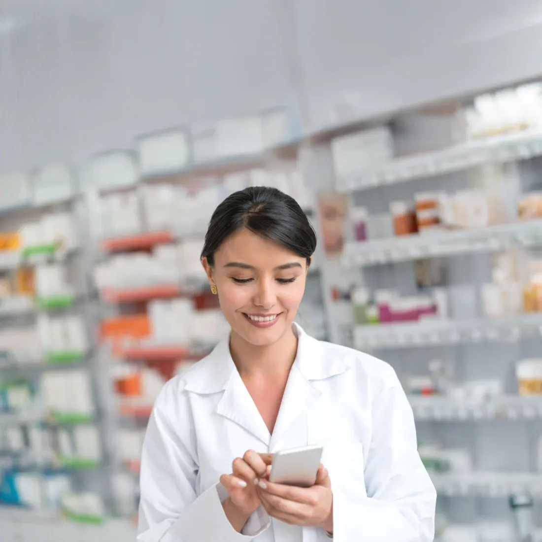 A smiling pharmacist checking her phone in her pharmacy